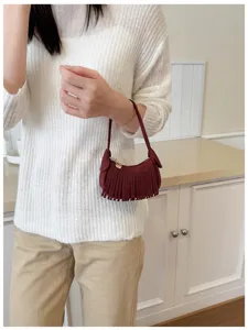 Burgundy suede-like fringe bag with a gold heart zipper pull, shown carried at the model's side