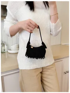 A black fringed mini bag held by hand, with a slim strap and small gold heart charm