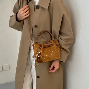 Sac cabas bandoulière marron à pois, avec anses et breloque, porté en travers sur un manteau