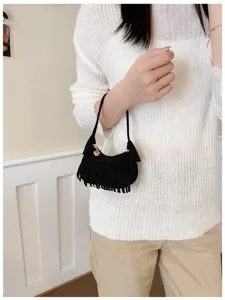 Model holding a small black suede-look bag with dense fringe, slim straps, and a gold heart charm