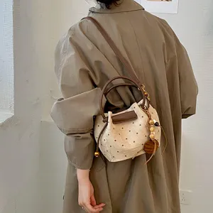 Sac seau à pois avec anses effet cuir marron et breloques, porté en bandoulière sur un manteau