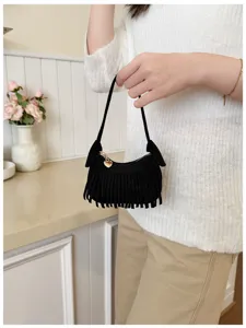 Lifestyle view of a woman holding a small black suede-look fringed bag with a gold heart clasp