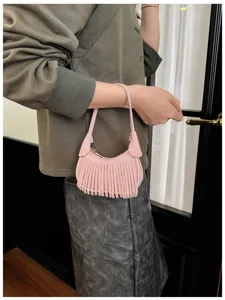 Close-up of a pink faux-suede crescent bag with long fringe and a slim handle, carried by hand