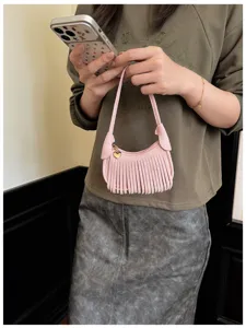 A person holds a small pink fringed bag with slim handles and a gold heart charm indoors