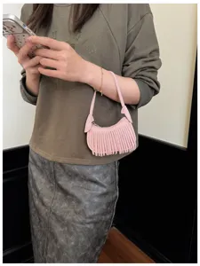 Pink fringed mini bag carried by hand in a neutral indoor setting, shown on a person