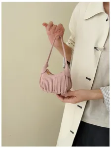 Person holding a pink suede-textured handbag with fringe trim, a short handle and gold-tone hardware