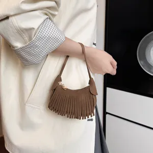 Brown suede-look mini fringe handbag with metal zipper, shown carried by hand in a casual outfit