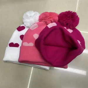 Three heart-pattern knitted beanies in white, pink and magenta, with pom-poms and folded cuffs