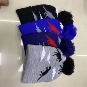 Flat lay of four dinosaur-pattern knit hats with pom-poms in black, blue, navy and gray
