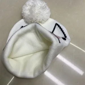 Close-up of the folded white knit hat lining, fluffy pom-pom, and partly visible black cat motif