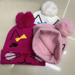 Three kids' knit hats in magenta, white and pink, with cat faces, cuffs and fluffy pom-poms