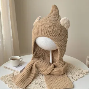 Camel knit hood and scarf displayed on a mannequin, showing pointed crown, ear details and pom-poms