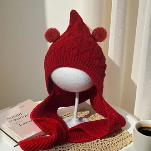 Close-up of a red cable-knit winter hat with pointed crown, twin pom-poms and long ties