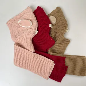 Flat lay of three cable-knit hooded neck warmers in pink, red, and camel with ribbed edges