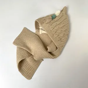 Close-up of camel knit texture, cable-knit hood, ribbed scarf, and three soft decorative pom-poms
