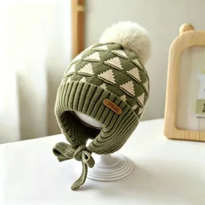 Close-up view of an olive green knit hat with cream triangle pattern, pom-pom and tied ear flaps
