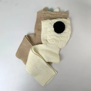 Flat lay of cream and camel knitted scarves with cable-knit panels, ribbed ends, and pom-pom accents
