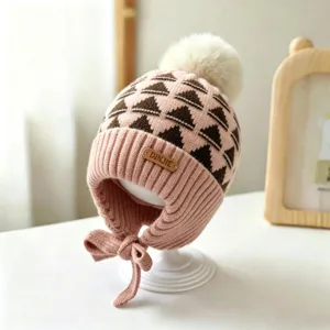 Close-up of a pink knit hat with brown geometric motifs, cream pompom and chin ties