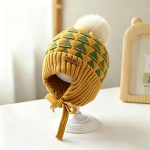 Yellow knit hat detail showing green triangles, white pom-pom, ribbed brim and chin ties