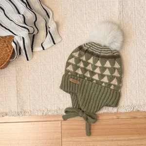 Flat lay of a green and cream knit hat with geometric pattern, fluffy pom-pom and tie ear flaps