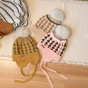 Three patterned knit hats in yellow, beige and pink, with fluffy pom-poms, ribbed cuffs and ties