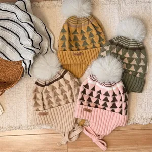 Four knitted children's hats with fluffy pom-poms and triangle patterns, laid out in warm colors