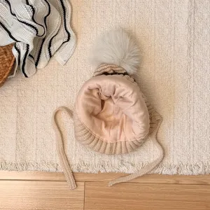 Top-down detail of a soft pink lining, beige knit edge, white pompom, and long ties