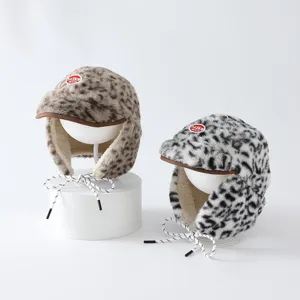Deux bonnets à rabats en peluche léopard, brun et noir et blanc, présentés sur des supports blancs