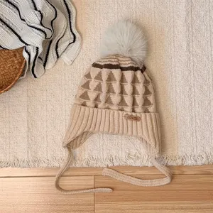 Flat-lay view of a beige children's knit hat with a triangular pattern, pom-pom and earflaps