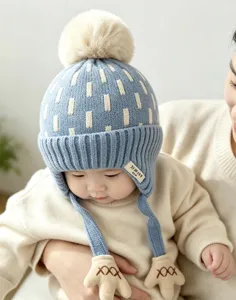 Baby wearing a blue knit hat with cream stripes, a fluffy pom-pom and bear-shaped ties