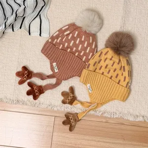 Flat lay of two children's knit hats with jacquard patterns, fluffy pom-poms and tied earflaps