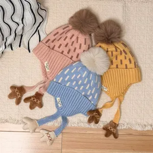Three kids' earflap knit hats in pink, blue and yellow, with pom-poms and bear-paw ties