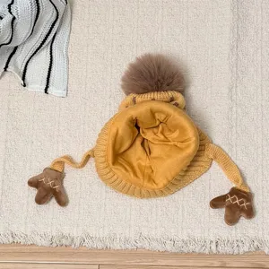 Flat lay showing the soft yellow lining, knit earflaps with brown bear-paw ties, and fluffy pompom