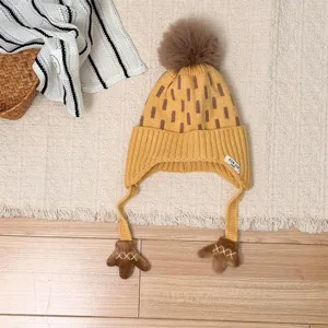 Overhead view of a yellow knit hat with brown stripes, fluffy pompom, earflaps and mitten ties