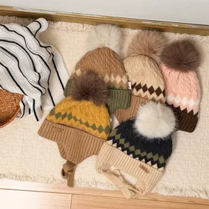 Flat lay showing patterned knit hats with pom-poms and earflaps on a cream woven rug