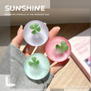 Hand houdt drie matte, doorschijnende bollen met klavermotieven vast in lila, roze en mintgroen