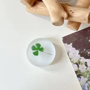 Close-up van een mat doorschijnend rond accessoire met een groen klavermotief op een wit tafelblad.