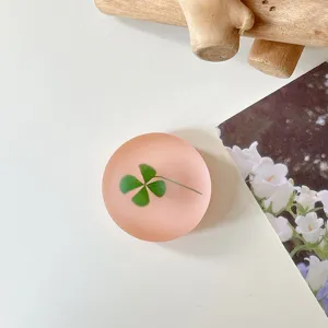 Close-up van een matte roze ronde telefoonhouder met een groen klavertje op een witte achtergrond