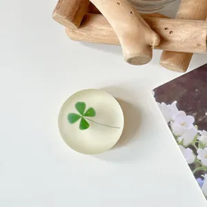 Bovenaanzicht van een ronde, matdoorzichtige telefoonhouder met een groen klavertjeviermotief