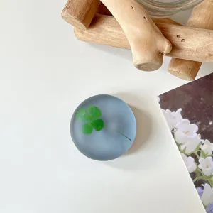 Close-up van een groen klavertje in een rond, mat blauwgrijs en doorschijnend decoratief object