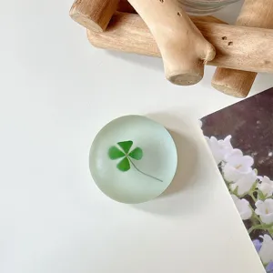 Close-up van een ronde, matte telefoonhouder met een groen klavermotief op een wit tafelblad