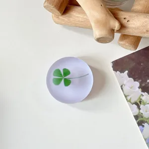 Close-up van een rond mat accessoire met een groene klaver, naast een boek met bloemenprint