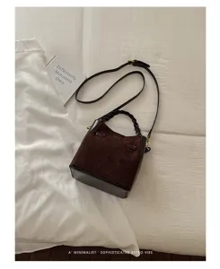 Flat lay of a dark brown suede and leather bag with braided handle, long strap and gold hardware