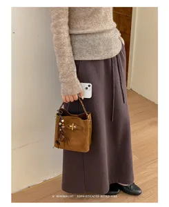 Brown suede-look bucket bag with drawstring closure, carried beside a long skirt in a retro outfit