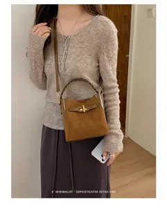 Model wearing a brown suede-textured bucket bag with woven handle and gold clasp
