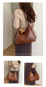 Lifestyle view of a brown bag with chain-and-leather strap, tassel and teddy bear charm