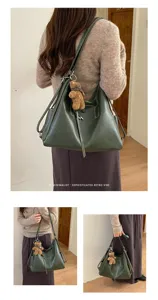 Lifestyle view of a woman carrying a dark green handbag with a teddy bear charm indoors