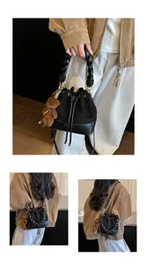 Model carrying a black bucket bag with a woven handle, drawstring closure and brown bear charm