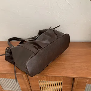 Vista oblicua de bolso marrón oscuro efecto piel, con textura, correa y tachuelas metálicas