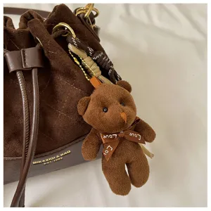 Close-up of a brown suede-look bag with diamond stitching and a plush bear charm hanging from it
